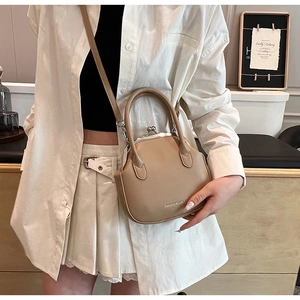 Detail of a beige clip bag with metal clasp worn with a white shirt and pleated skirt