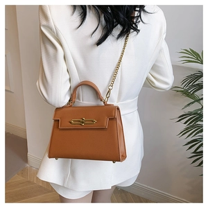 Detalle de bolso Saffiano marrón caramelo con cierre dorado y cadena sobre blazer blanco