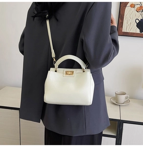 Detail of a minimalist cream white leather handbag featuring a golden swivel lock and strap