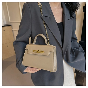 Detalle de bolso beige en cuero granulado con correa de cadena dorada y cierre metálico