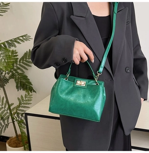 Close-up of a vintage green leather handbag with a gold twist-lock on a grey blazer