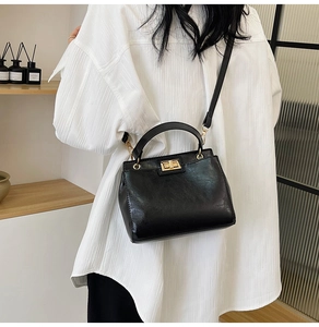 Detail of black faux leather handbag featuring a golden buckle and adjustable shoulder strap