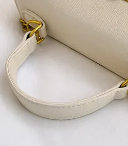 Detalle del asa de cuero Saffiano blanco con hebilla dorada de un bolso bandolera