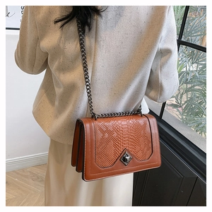 Detail of orange brown crocodile pattern leather bag with metallic chain and clasp