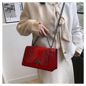 Detail of red crocodile pattern shoulder bag with metal chain strap on model wearing tweed