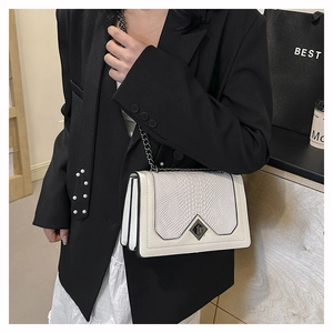 Detail of white crocodile embossed crossbody bag with metal chain on a female model