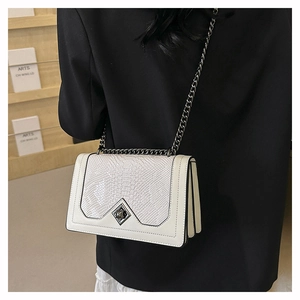 Detail of white crocodile embossed leather bag with silver buckle worn on black blazer