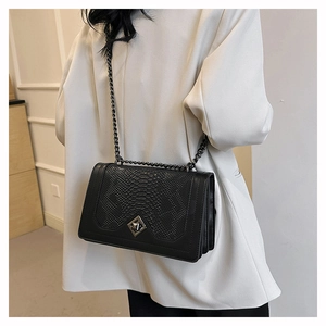 Detail of black shoulder bag featuring textured scales and sleek metallic chain strap