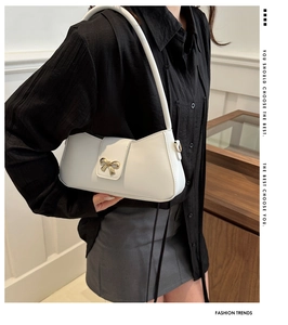 Detail shot of a white PU leather shoulder bag featuring a gold bow metallic buckle detail