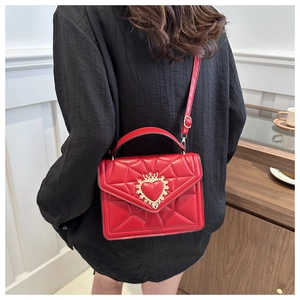 Detail of red quilted crossbody bag featuring a golden crown heart buckle and leather texture