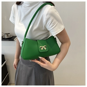 Detail of green baguette underarm bag featuring a gold bow buckle and leather texture