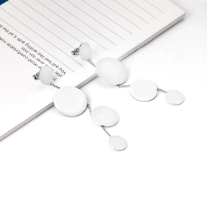 Macro shot of silver geometric round disc tassel earrings on a white notebook surface