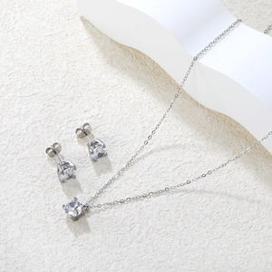 Elegant four-claw zircon necklace and earrings set on a white stone minimalist surface