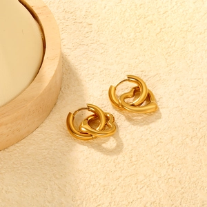 Golden double-loop heart earrings with interlocking rings on a textured beige surface