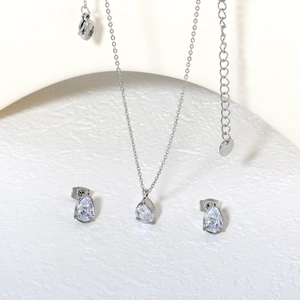 Elegantes Set aus Silberhalskette und Zirkonia-Ohrsteckern auf weißem, schlichtem Sockel