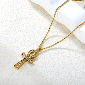 Collier pendentif croix Ankh doré avec cristaux clairs sur une surface en pierre texturée