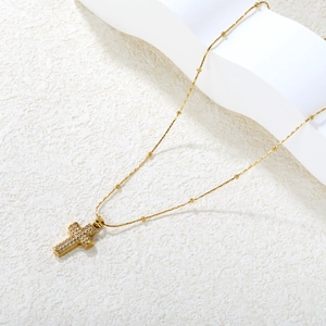Elegant gold cross necklace with pavé zircon pendant on a textured stone surface