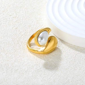 Top view of a gold-plated open ring with a large white pearl on a textured surface