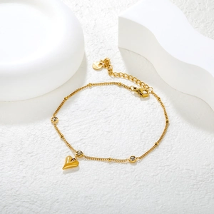 Golden butterfly tassel anklet with heart pendant and white zircon on white stone background