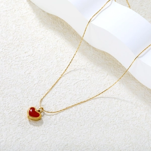 Elegant gold chain necklace with red heart pendant on a minimalist white textured backdrop