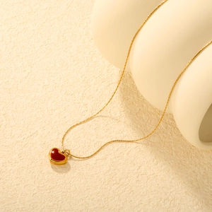 Elegant gold chain necklace featuring a red enamel heart pendant on a ceramic stand