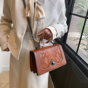 Brown crocodile embossed flap crossbody bag with metal chain strap worn by a female model