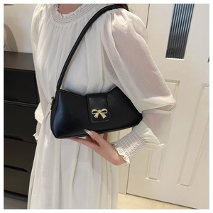 Detail of black matte leather underarm bag with gold bow clasp on white dress
