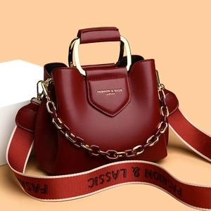 Deep red leather bucket bag with square gold metal handle and wide woven shoulder strap