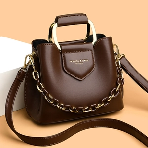 Deep brown polished leather bucket bag with gold chain and handle on orange background