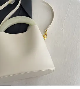Détail d'un sac seau en cuir crème avec poignée en résine verte et finitions dorées