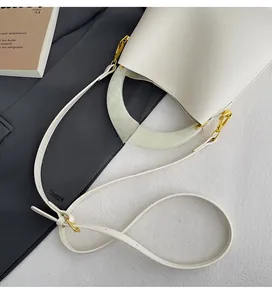 Détail d'un sac seau en cuir blanc avec poignée en résine marbrée et bandoulière dorée