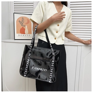 Detail of black glossy tote bag featuring white FASHION print and woven letter straps