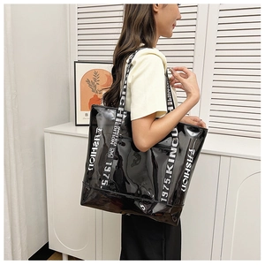 Side view of large black glossy tote bag featuring white bold letters and wide canvas strap