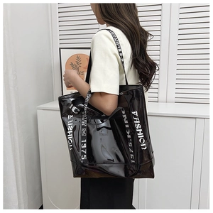 Detail of high-gloss black tote bag with white FASHION lettering and wide shoulder strap