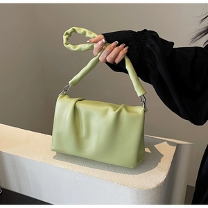 Close-up of pistachio green pleated handbag with twisted handle and silver metal hook