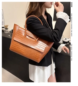 Brown crocodile embossed leather tote bag shown in a professional lifestyle setting