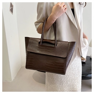 Detail of a large brown crocodile-embossed tote bag worn by a model in a minimalist setting