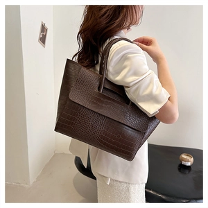 Close-up of a large dark brown crocodile pattern tote bag held by a model