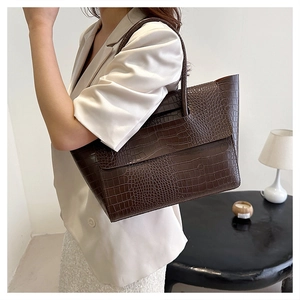 Detail of dark brown crocodile-embossed leather tote bag showing texture and handle
