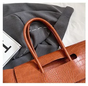 Detailed close-up of brown crocodile texture and sturdy handles on a stylish tote bag