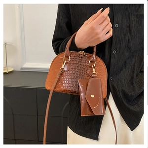 Detail of a dark brown crocodile embossed shell bag with matching mini charm and gold hardware