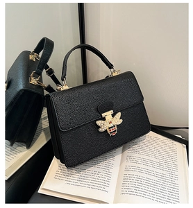 Detail der schwarzen Handtasche aus Leder mit goldener Bienenschließe auf einem Buch