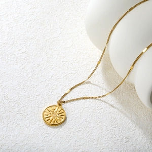 Collier en acier doré avec pendentif pièce soleil sur un support blanc décoratif