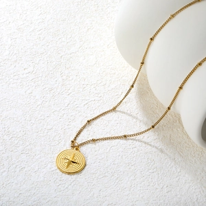 Collier doré étoile à huit branches avec chaîne à perles sur un présentoir en céramique