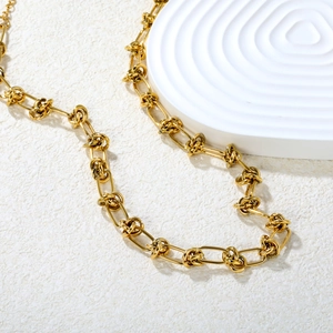 Gold knot link necklace in stainless steel displayed on a white textured pedestal