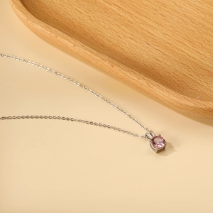 Macro detail of round pink gemstone pendant with four-prong setting on silver chain