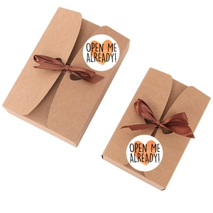 Brown kraft paper gift box with silk bow and Open Me Already sticker label on white background