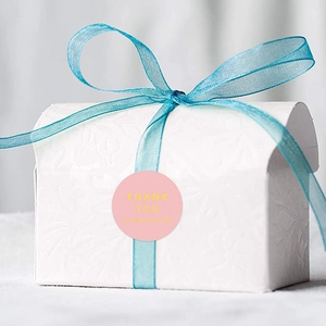 Pink round Thank You sticker on white embossed gift box with blue organza ribbon bow