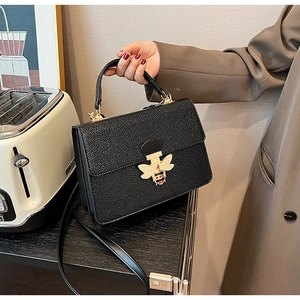 Detail der goldenen Bienenschnalle mit Perlenflügeln auf schwarzer Lederhandtasche