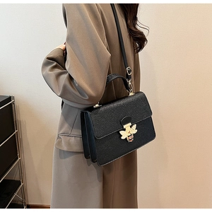 Detail einer schwarzen Lederhandtasche mit goldenem Bienenverschluss und Emaille-Akzenten